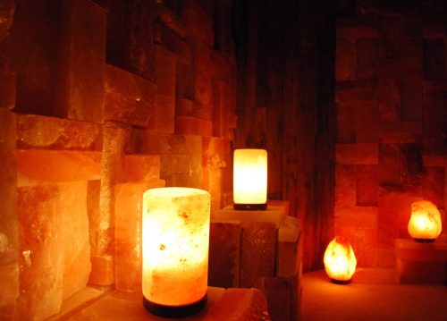 Warm, glowing salt lamps illuminate a cozy, rustic room with salt brick walls.