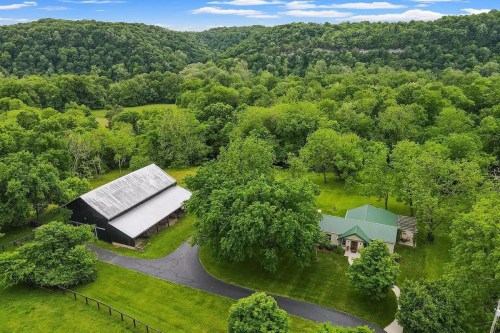 Aerial view of a green landscape featuring a house and barn surrounded by lush trees and rolling hills.