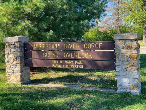 Sign for Mississippi River Gorge Scenic Overlook, located in Saint Paul, with stone pillars and green surroundings.