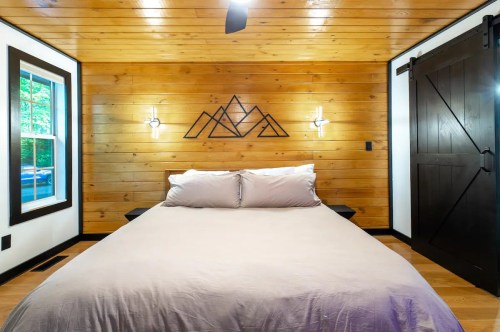 Cozy bedroom with wooden walls, a bed with gray bedding, and a mountain-themed wall decoration.