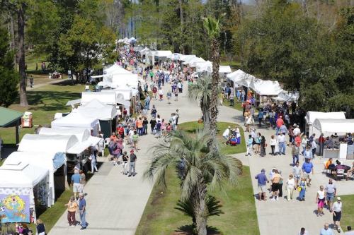 Aerial view of a bustling outdoor festival with white tents, vendors, and crowds enjoying the event in a park setting.