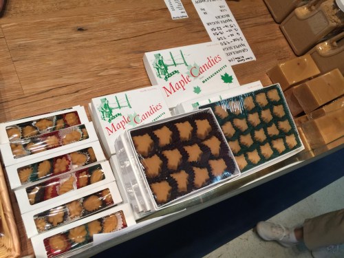 Assorted maple candies in various shapes and colors displayed in boxes on a wooden table.