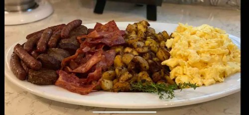 A platter featuring sausages, bacon, seasoned potatoes, and scrambled eggs, garnished with fresh thyme.