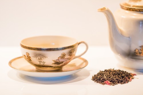 A delicate tea cup and saucer beside a teapot, with loose tea leaves scattered on the surface.