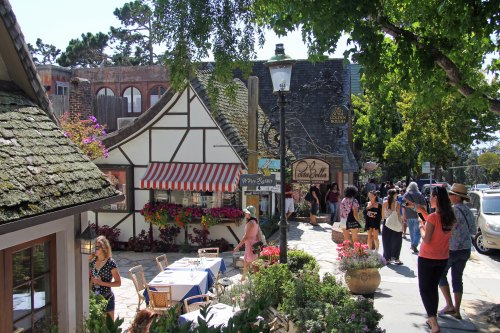 A charming street scene with quaint shops, colorful flowers, and people strolling in a sunny, vibrant setting.