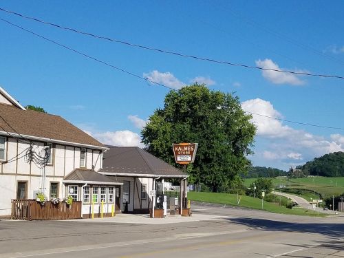 A small town scene featuring a building with a sign for "Kalmes Store," surrounded by green hills and blue skies.