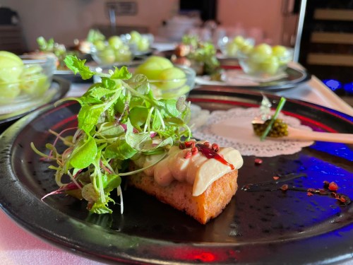A gourmet dish featuring a crispy base topped with creamy sauce, fresh greens, and a drizzle of sauce on a black plate.