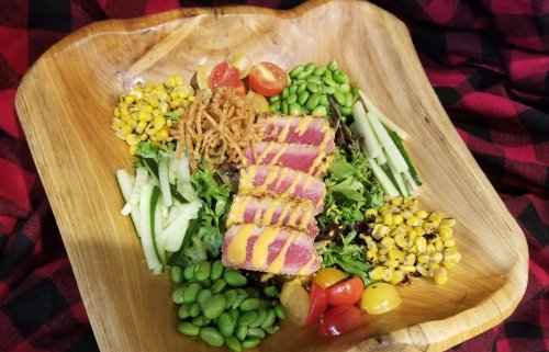 A wooden bowl filled with salad, featuring seared tuna, mixed greens, cherry tomatoes, corn, and edamame.
