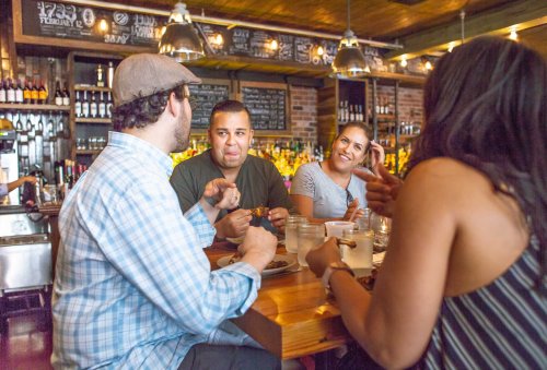 A group of four friends enjoying a meal and drinks at a cozy restaurant, engaged in lively conversation.