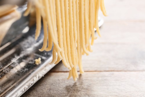Freshly made pasta strands hanging from a pasta machine, resting on a wooden surface.