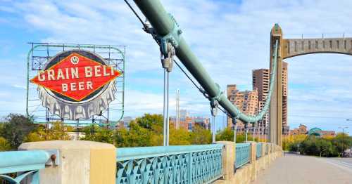 A bridge with a large "Grain Belt Beer" sign in the background, surrounded by city buildings and trees.