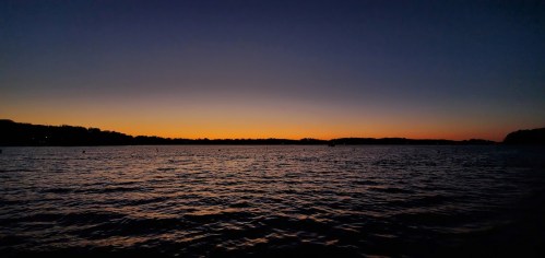 A serene lake at sunset, with a gradient of orange and blue hues reflecting on the water's surface.