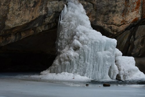 A large, frozen ice formation stands near a rocky cave, surrounded by a frozen lake.