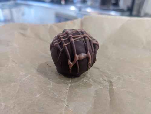 A chocolate truffle drizzled with caramel on a piece of parchment paper.