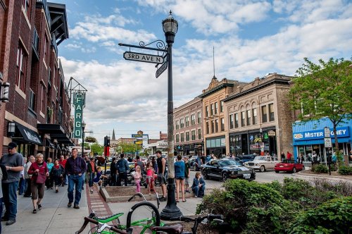 A bustling street scene in Fargo, featuring shops, pedestrians, and vintage signage under a partly cloudy sky.