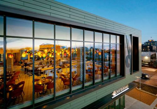 Modern restaurant exterior with large windows reflecting colorful lights and a city skyline at dusk.