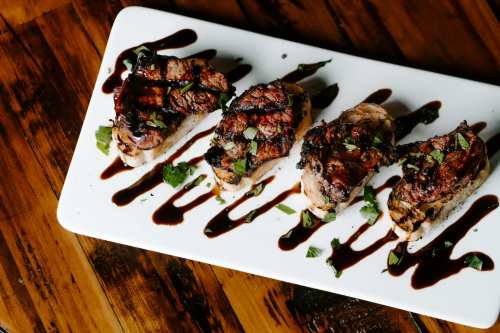 Grilled meat skewers on toasted bread, drizzled with balsamic glaze and garnished with fresh herbs on a white plate.
