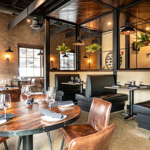 Modern restaurant interior featuring wooden tables, leather chairs, and greenery, with a warm, inviting atmosphere.