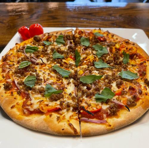 A freshly baked pizza topped with sausage, peppers, onions, and fresh basil, served on a white plate.