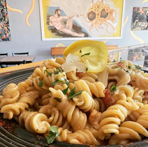 A plate of creamy pasta with lemon and herbs, set against a colorful mural featuring a whimsical interpretation of a classic artwork.