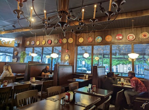 Cozy restaurant interior with wooden booths, chandeliers, and decorative plates on the walls. Patrons dining at tables.