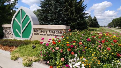 Sign for McCrory Gardens at South Dakota State University, surrounded by colorful flowers and greenery under a blue sky.