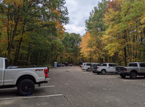 A parking lot surrounded by trees with autumn foliage, featuring several parked trucks and vehicles.