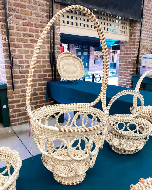 A handcrafted woven basket with a tall handle, displayed on a table in a market setting.