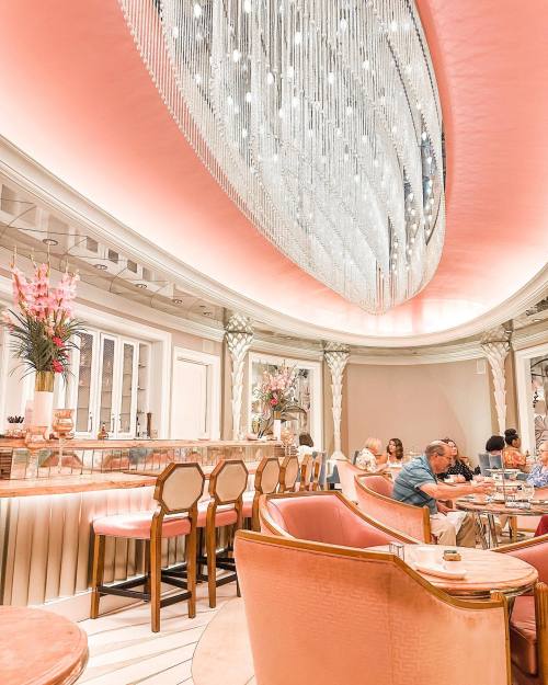 Elegant restaurant interior with pink lighting, a chandelier, and patrons enjoying their meals at stylish tables.