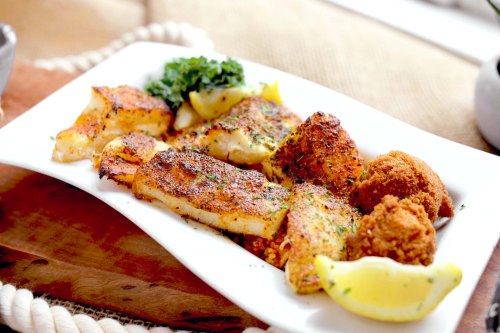 A plate of seasoned fish fillets with lemon wedges and a side of crispy fritters, garnished with greens.