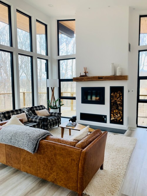 Cozy living room with large windows, a fireplace, and stylish furniture, featuring a mix of textures and natural light.