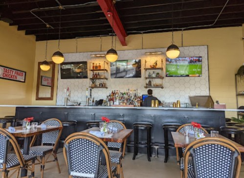 Interior of a restaurant featuring a bar, tables with flowers, and a TV displaying a sports game.