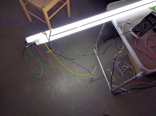 A fluorescent light fixture with multiple colored wires connected, resting on a table in a workshop setting.