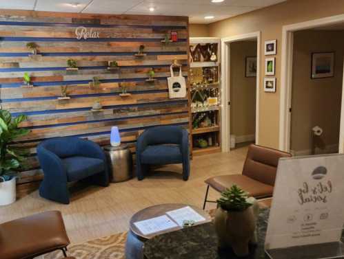 Cozy waiting area with blue chairs, wooden accent wall, plants, and a calming atmosphere.