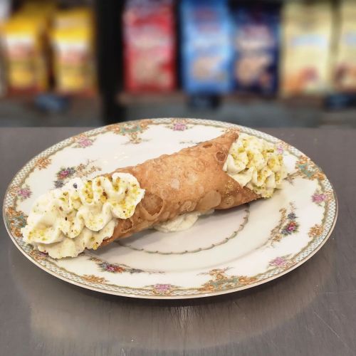 A beautifully plated cannoli filled with cream and topped with whipped cream, set on an ornate floral plate.
