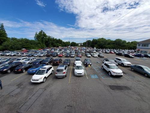 Aerial view of a crowded parking lot filled with numerous cars under a partly cloudy sky.