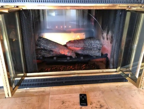 A cozy fireplace with glowing logs and a remote control on the floor in front of it.