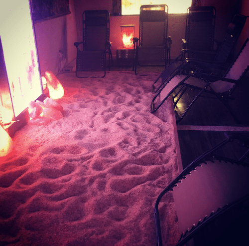 A cozy room with a sandy floor, lounge chairs, and glowing salt lamps, creating a relaxing atmosphere.