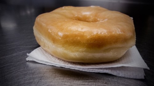A glazed donut resting on a white napkin on a metal surface.