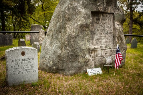 Gravestones of John Browne and a memorial stone in a cemetery, with an American flag and greenery in the background.