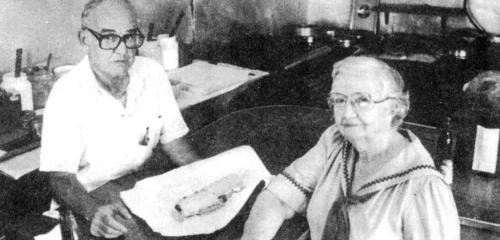 A black and white photo of an older man and woman sitting at a table with a rolled dish in front of them.