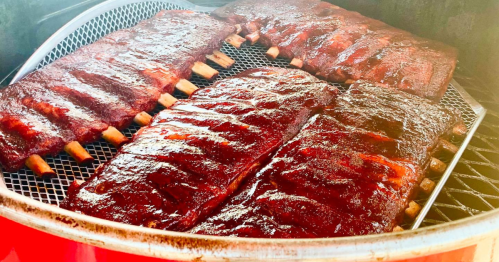 Four racks of glazed barbecue ribs cooking on a smoker, showcasing a rich, caramelized exterior.
