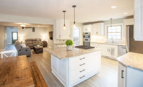 Bright, modern kitchen with white cabinets, granite countertops, and an island, overlooking a cozy living area.