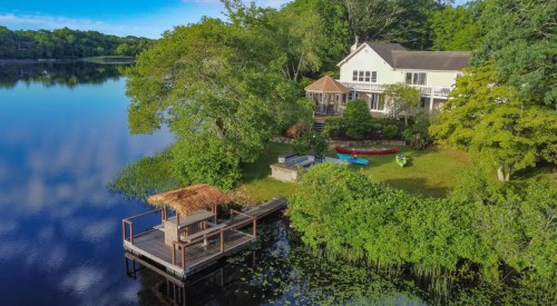 A serene lakeside home with a dock, surrounded by lush greenery and colorful kayaks on the water.