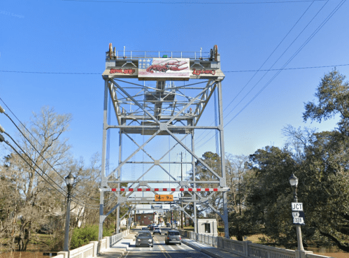A drawbridge with a large sign featuring a crawfish, surrounded by trees and vehicles approaching the bridge.