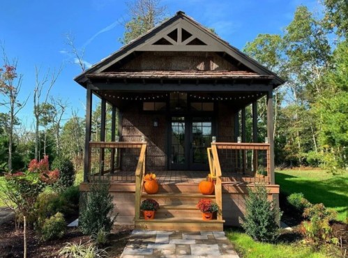 Charming cottage with a porch, pumpkins, and greenery, set against a clear blue sky.