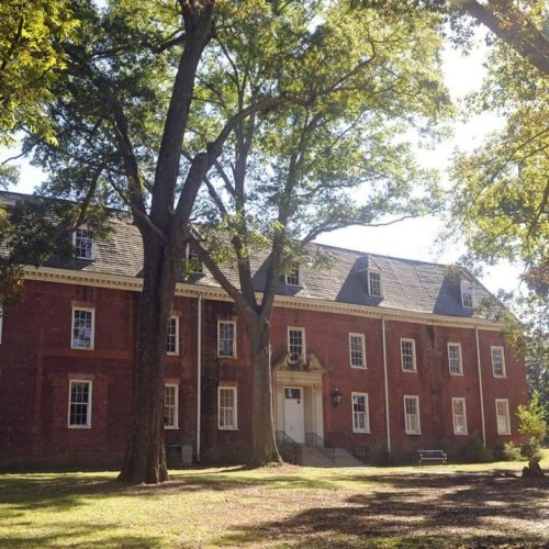 A red brick building surrounded by large trees and a grassy area, with a clear blue sky above.