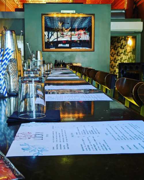 A long dining table set with glasses and menus, featuring a framed artwork on the wall in a stylish restaurant.