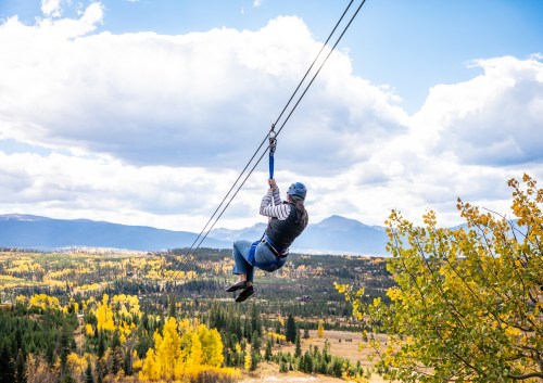 A person zip-lining over a colorful autumn landscape with mountains and trees in the background.