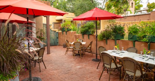 A garden patio with bistro tables under red umbrellas at a New Mexico restaurant.